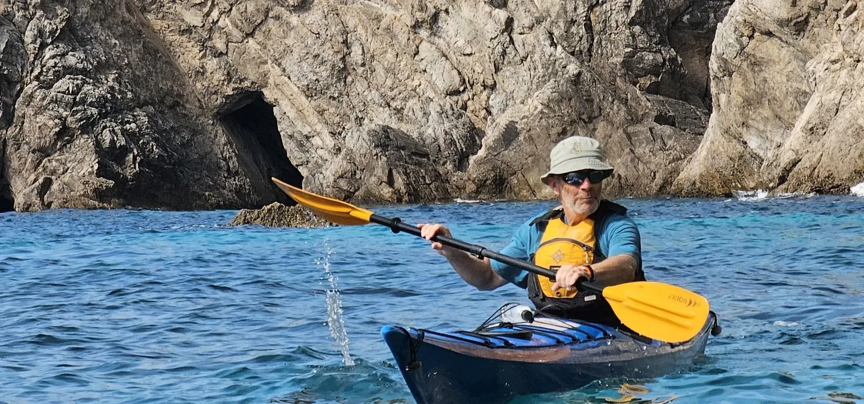 A kayaker paddling past a sea cave in a rocky cliff