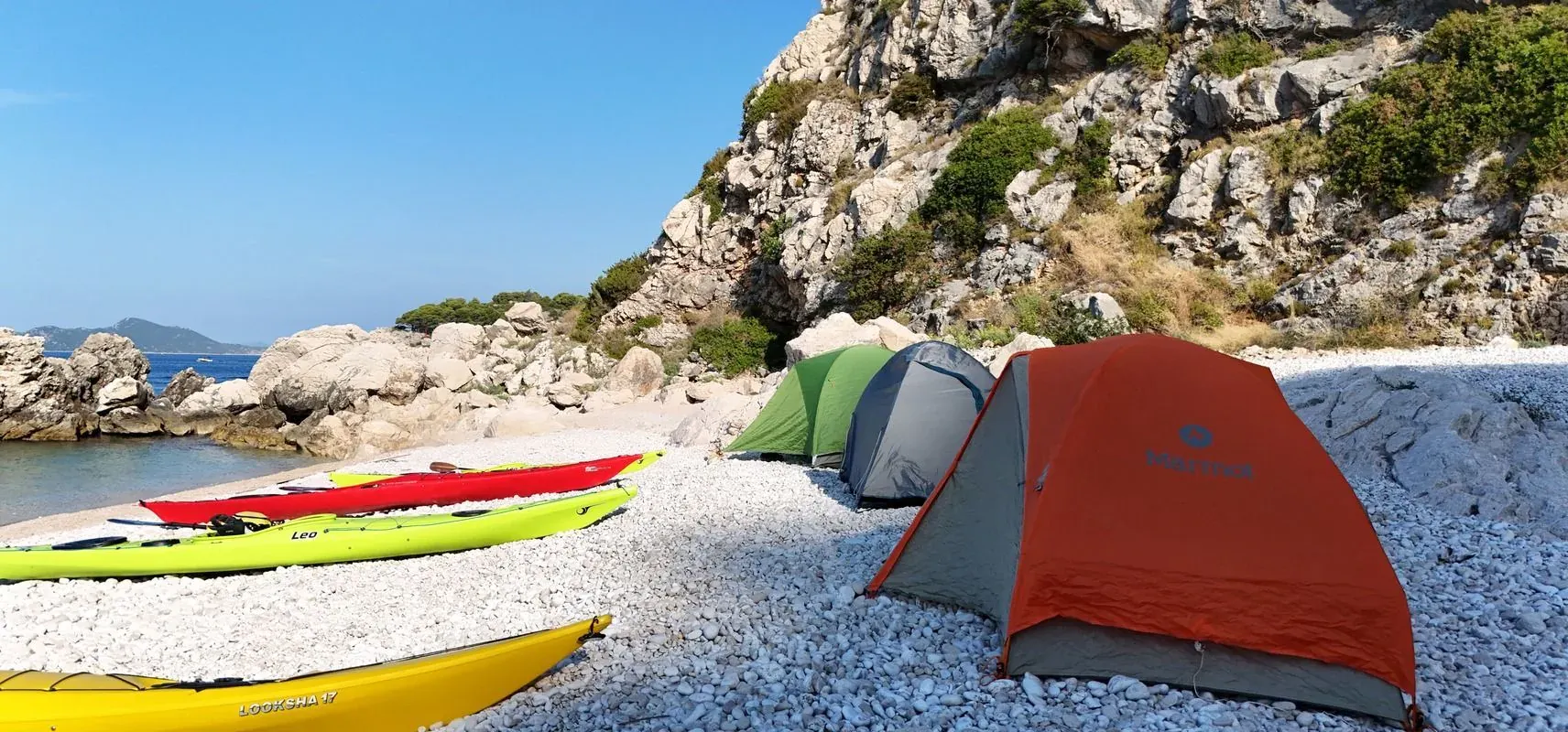 Sea kayaks and tents on a pebble beach below a rocky headland