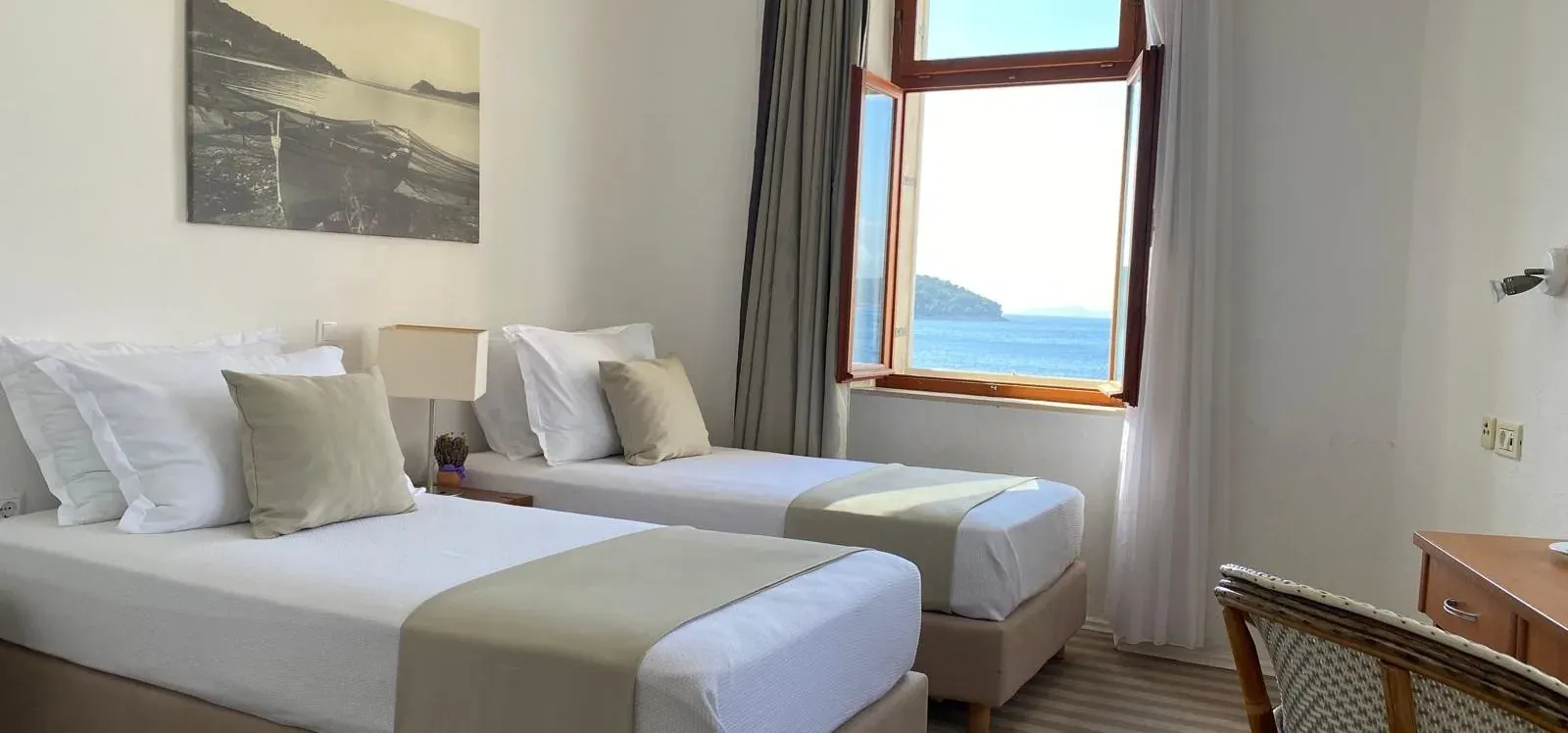 Twin beds in a bright island guesthouse room with a sea view through the window