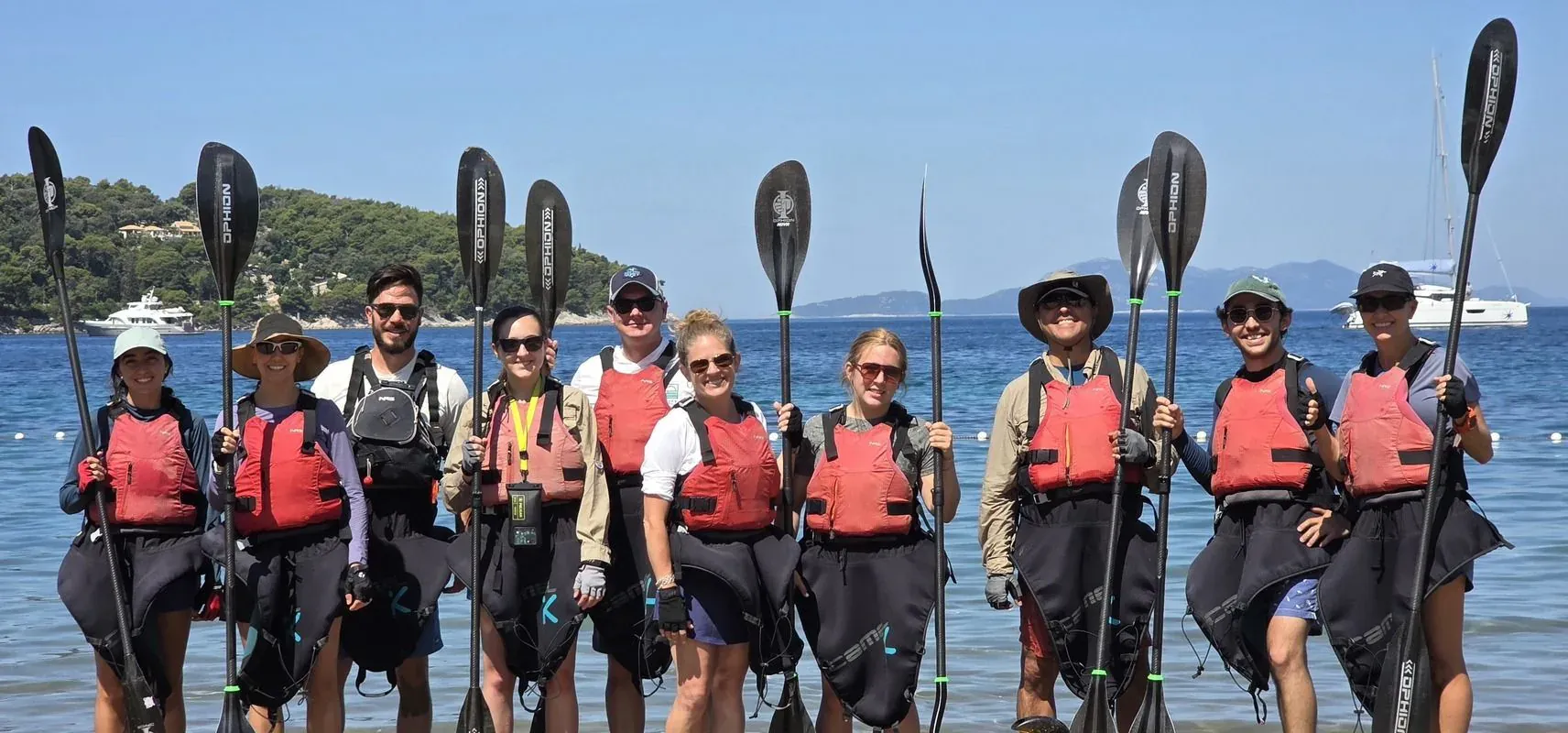 A kayak club group standing in shallow water holding their paddles upright