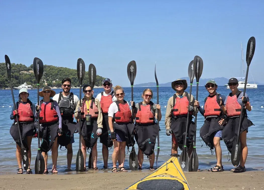 A group of kayakers standing with paddles raised on a beach