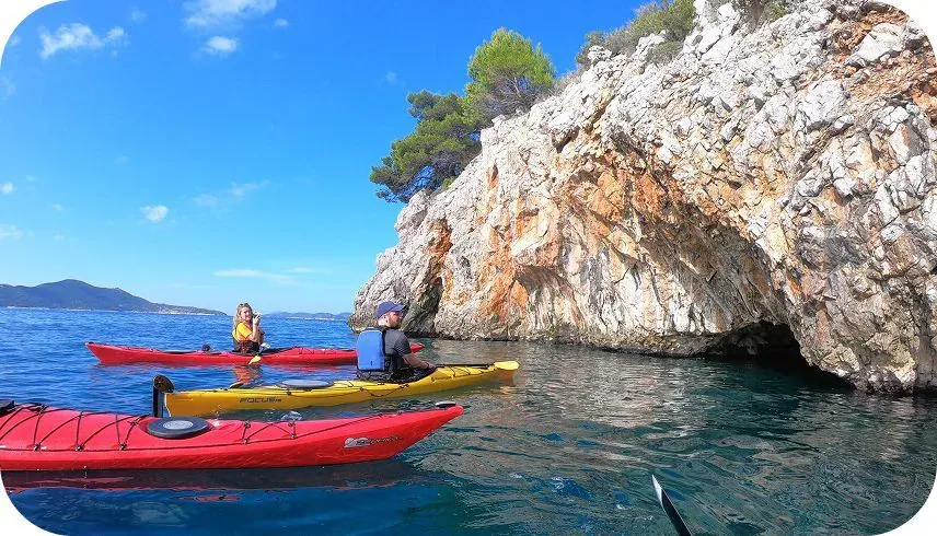 Red and yellow sea kayaks resting beside a limestone cliff on calm water