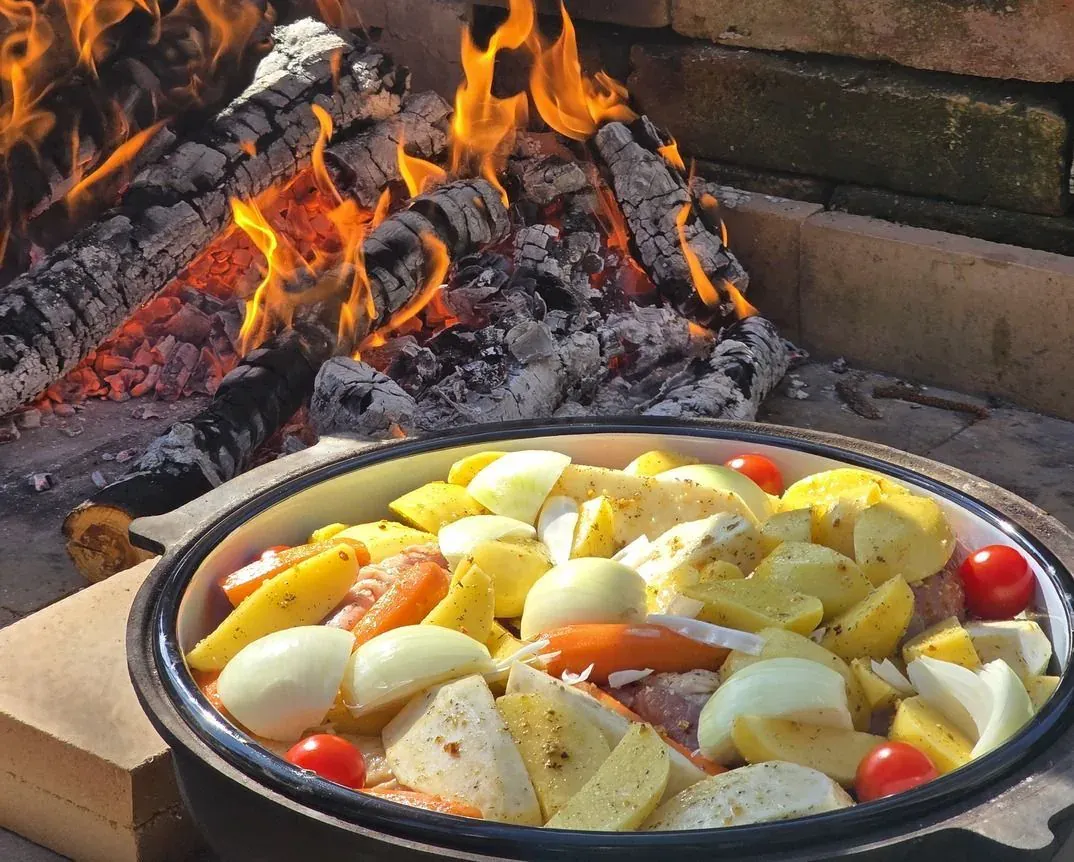 A peka of potatoes and vegetables cooking beside an open fire