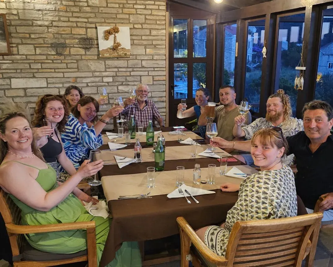 A tour group raising their glasses around a long dinner table