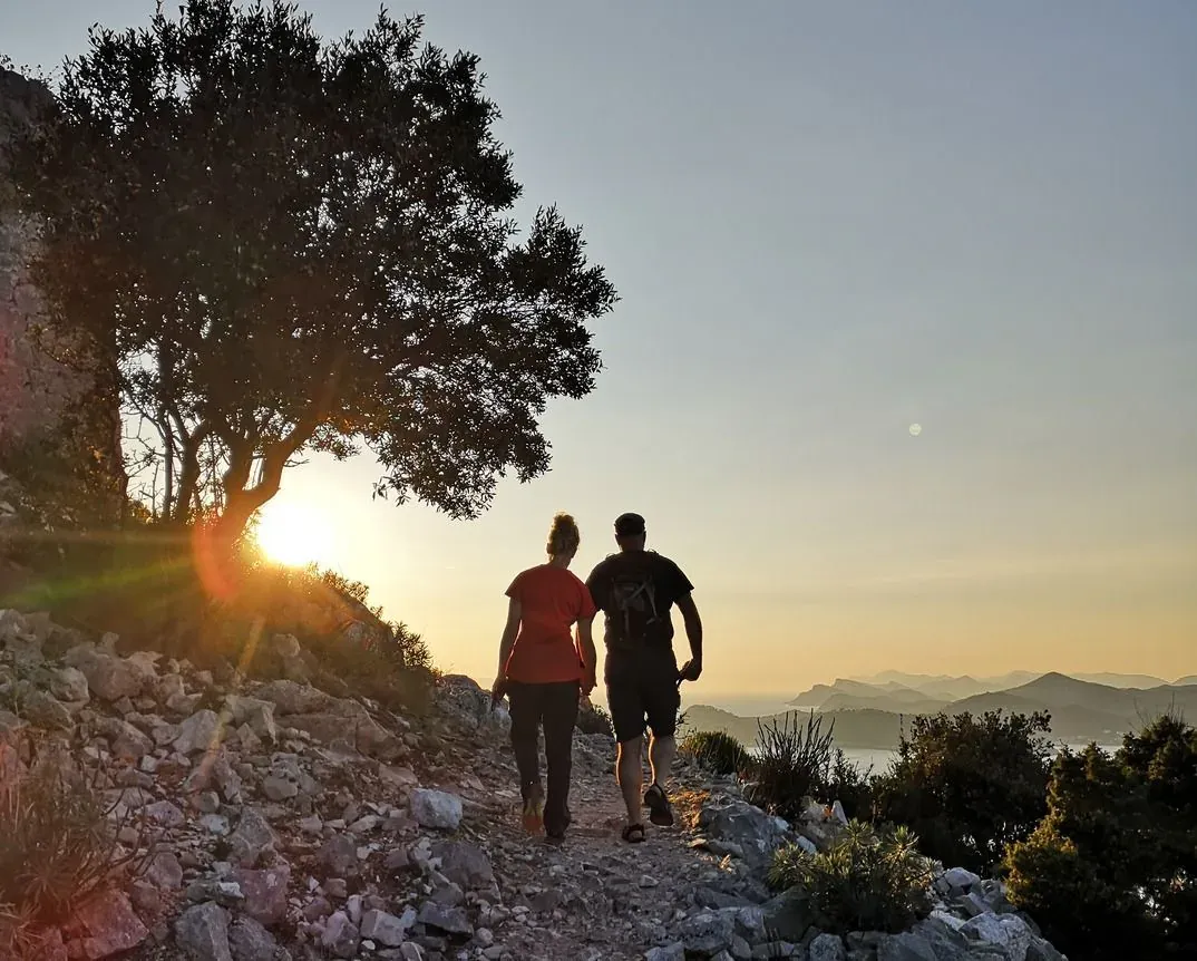 Two hikers walking a rocky ridge trail at sunset
