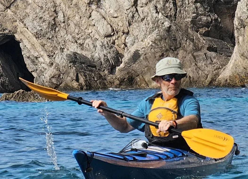 A kayaker paddling past a rocky cliff on a calm day
