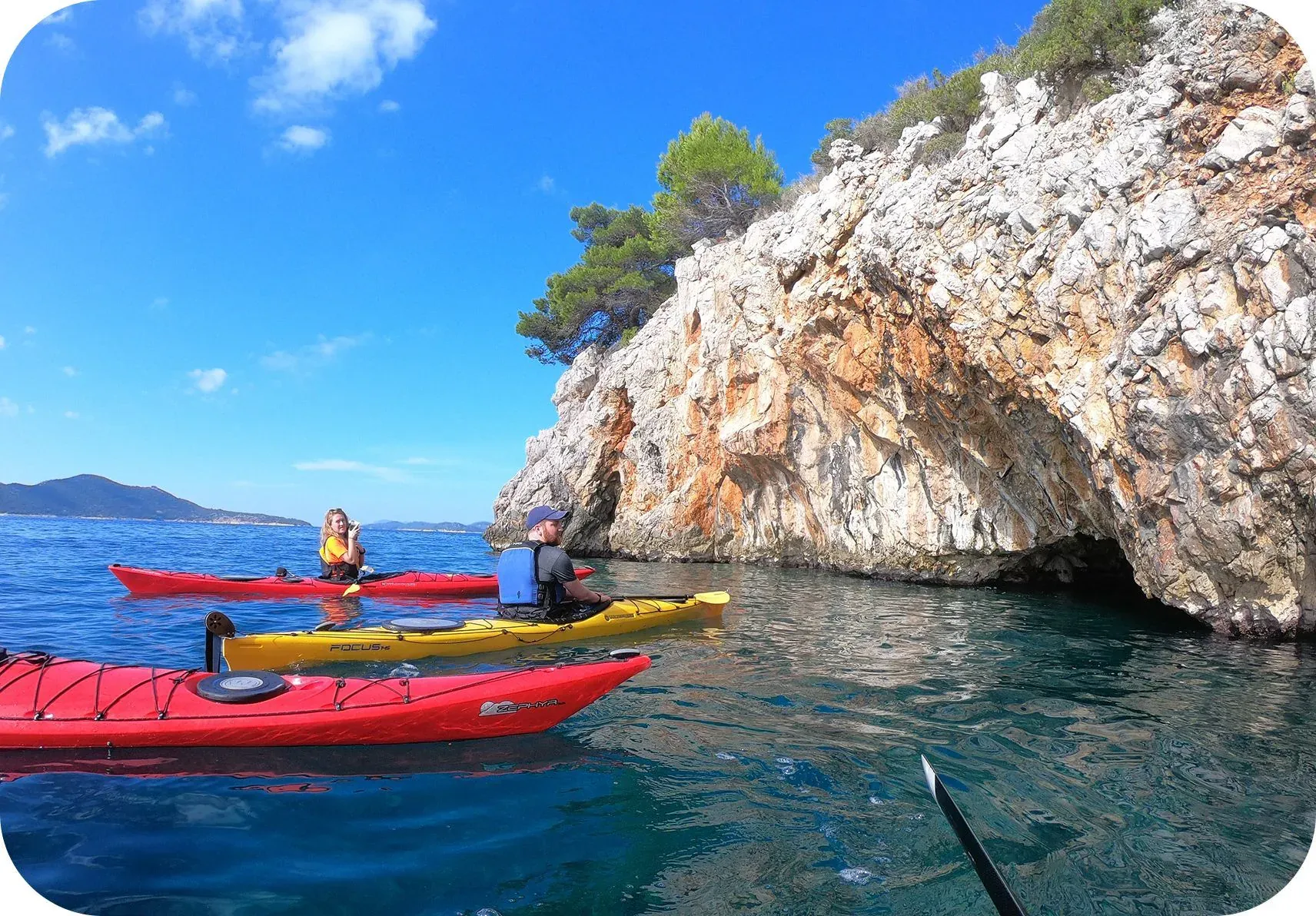 Sea kayaks moored below a pine-topped limestone cliff on the Adriatic coast