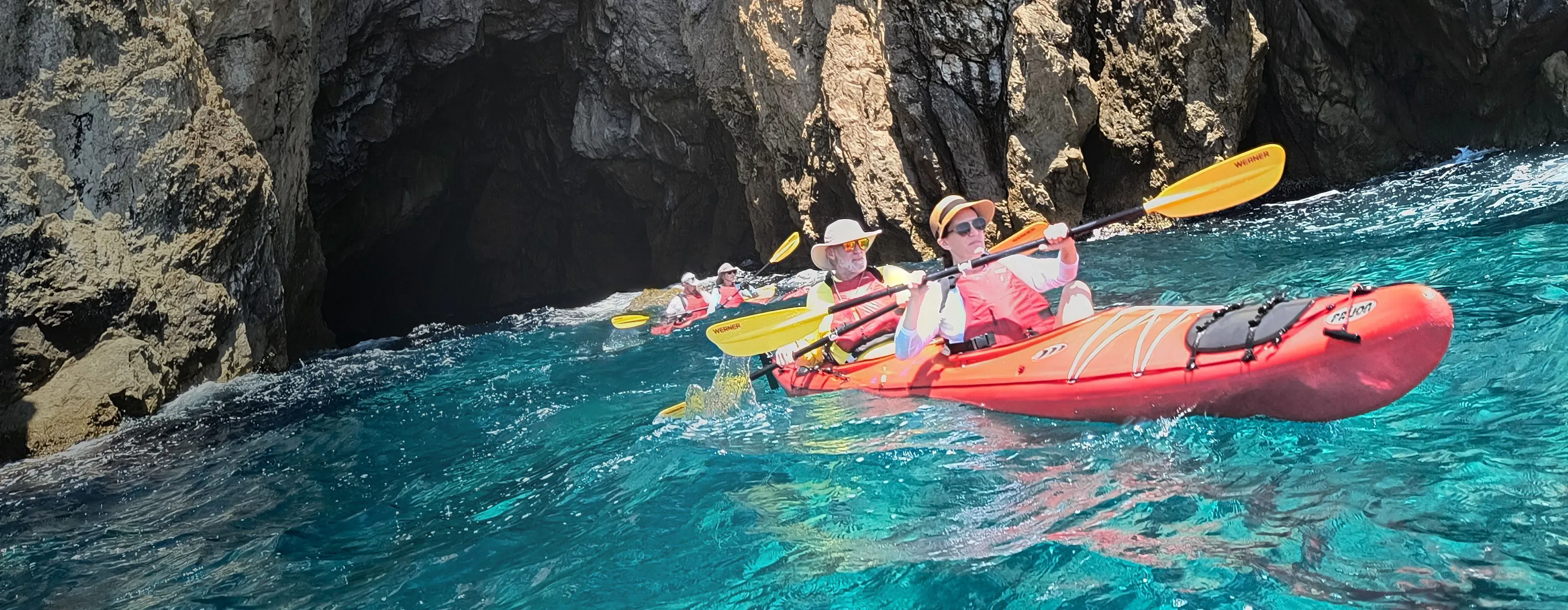 Group of kayakers paddling past a sea cave in clear turquoise water