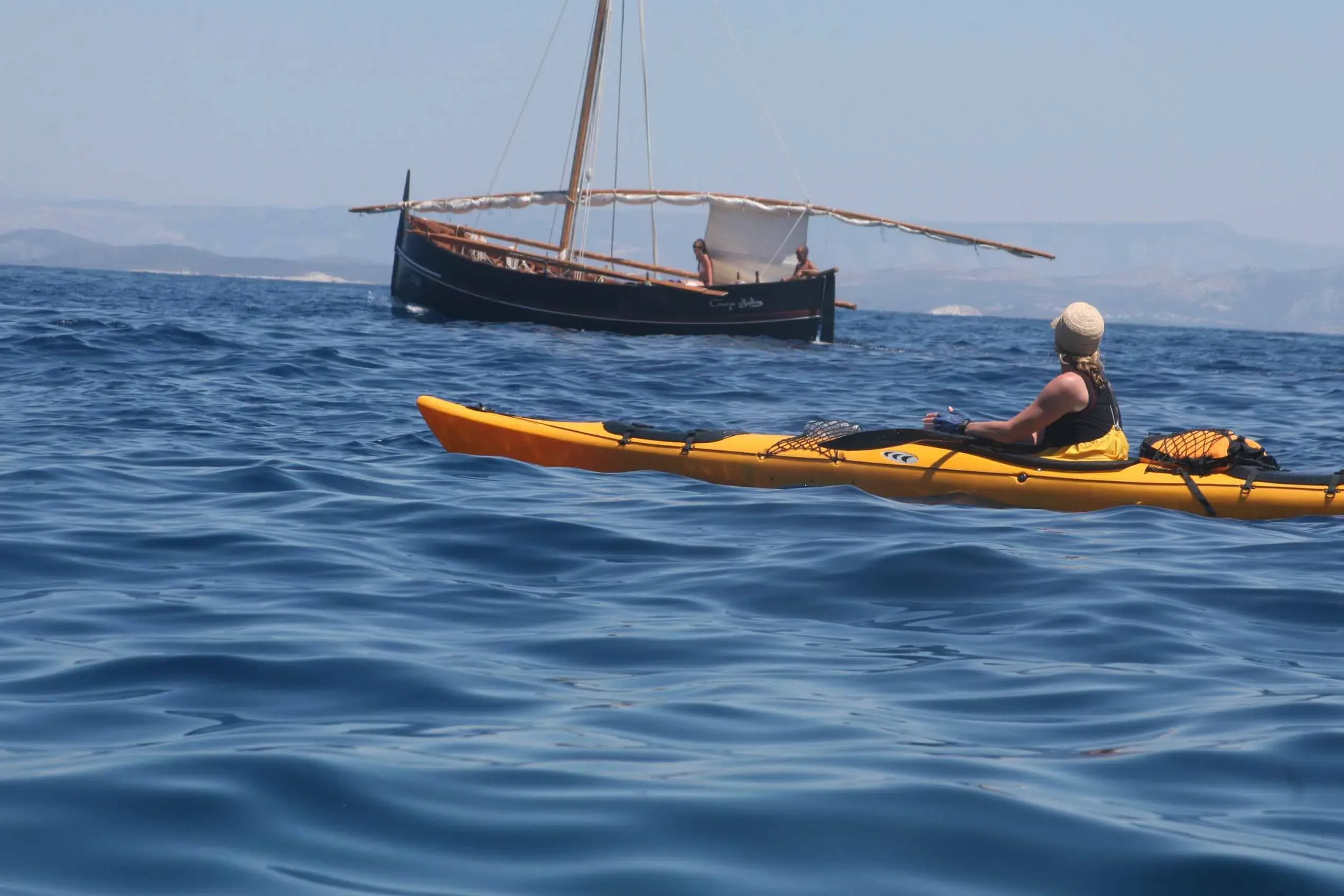 A sea kayaker paddling past a traditional wooden sailing boat off Vis