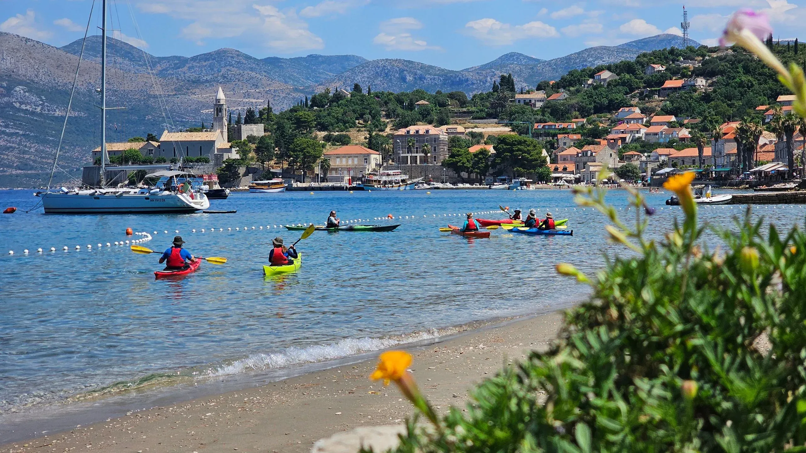 Colourful kayaks setting off from a beach below a Dalmatian village
