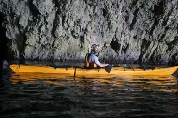 A kayaker in a yellow sea kayak inside a dimly lit sea cave