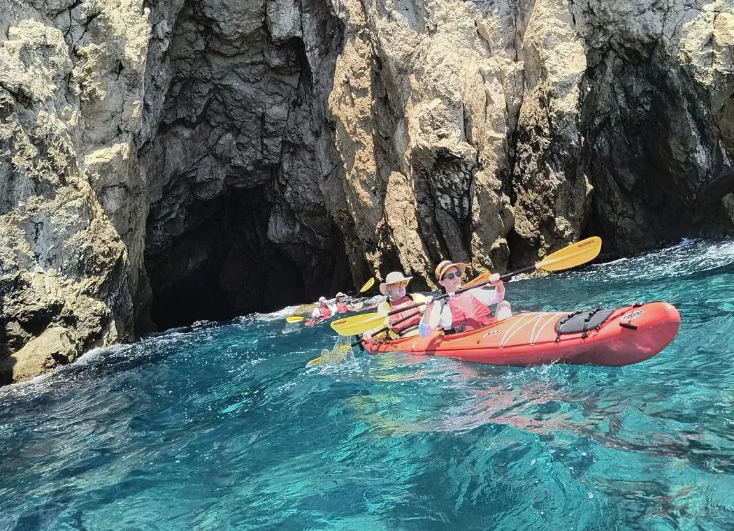 Kayakers at the mouth of a sea cave in choppy turquoise water