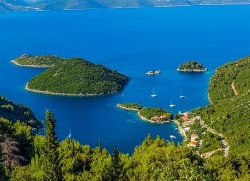Aerial view of wooded islets and moored yachts in a deep blue bay