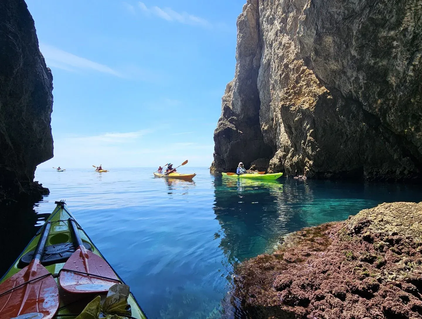 Kayakers gliding through a narrow channel between tall limestone cliffs on glassy blue water