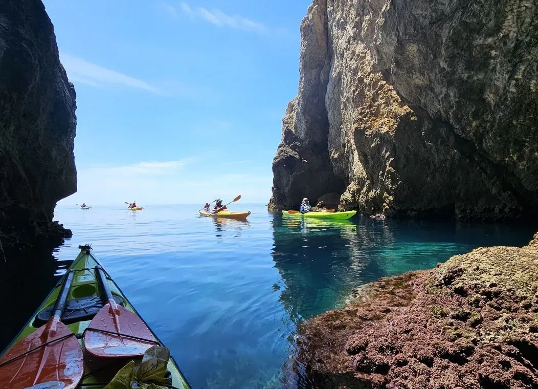 Kayakers paddling through turquoise water beside a limestone cliff