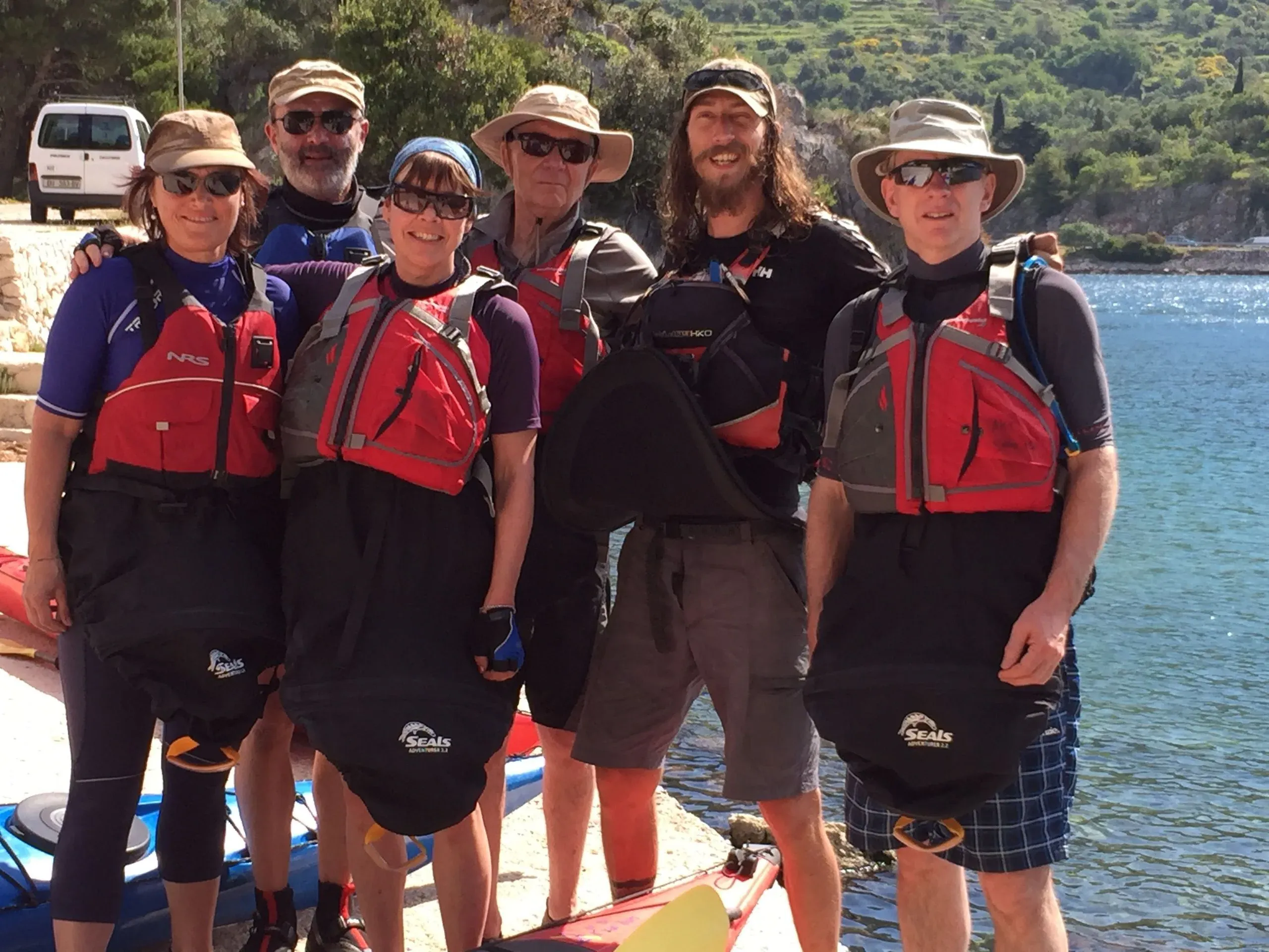 Six kayakers in buoyancy aids and spray decks gathered on the shore before a paddle