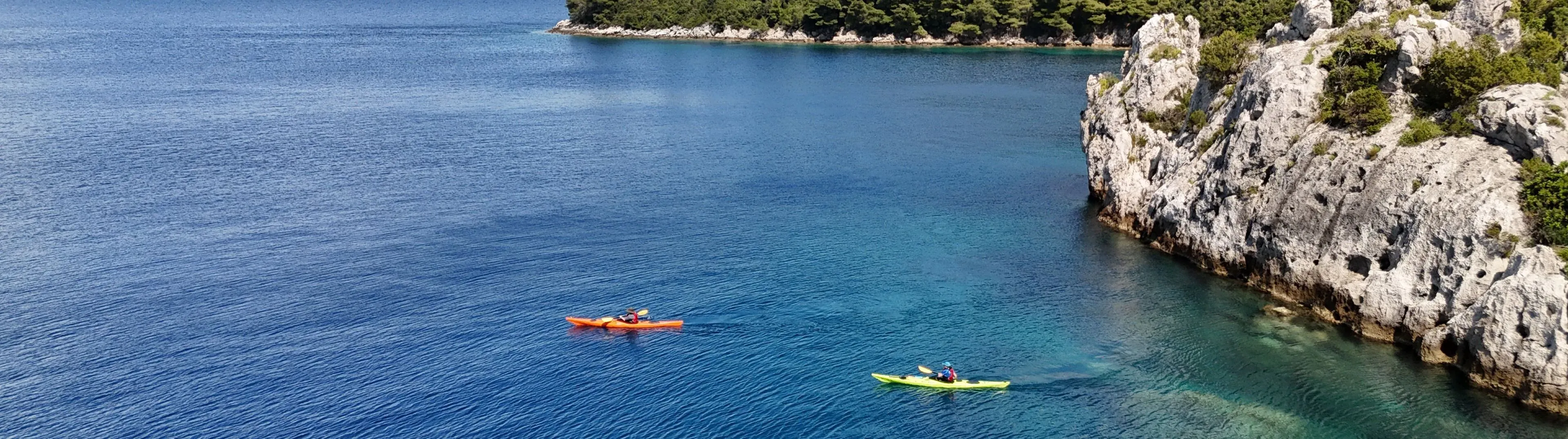 Kayakers on deep blue water beside a wooded limestone island
