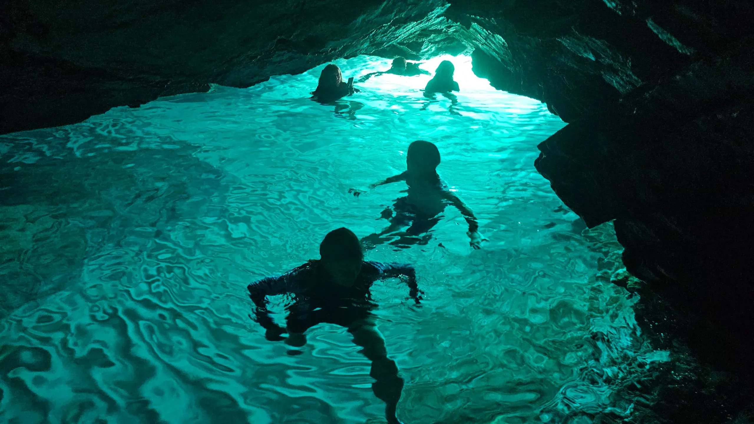 Swimmers in the turquoise water inside a sea cave